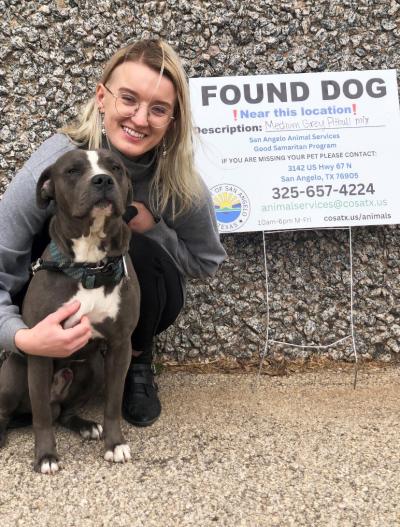 Smiling person hugging a black and white dog with a Good Sam program Found Dog sign behind them