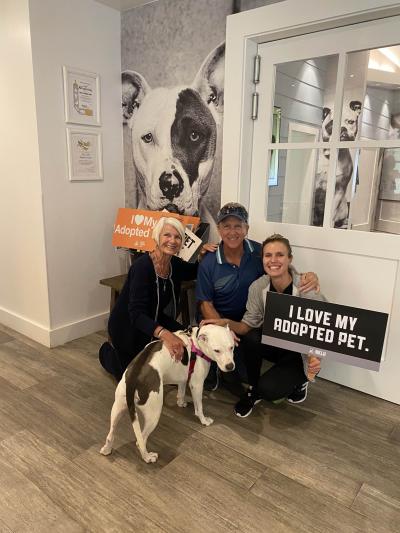 Spots the dog getting adopted from the Best Friends Pet Adoption Center in Los Angeles with three people, one holding a sign that says, "I love my adopted pet"