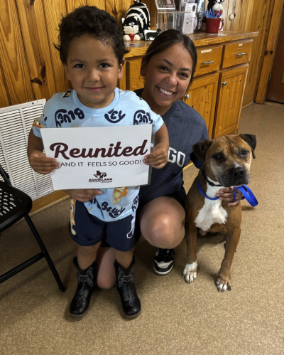 Childing holding a "Reunited" sign beside a smiling woman and dog