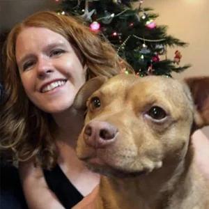 Michaelann Nelson with a dog in front of her and a Christmas tree behind