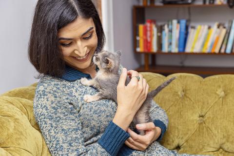 Smiling person cradling a dilute kitten on a couch in front of some books