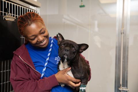 Shelter employee smiling at dog in her arms.