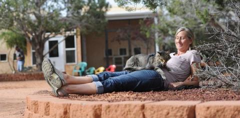 Woman lying in sand with cat on abdomen