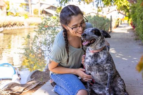Young woman smiling warmly at her dog along a sunny canal.