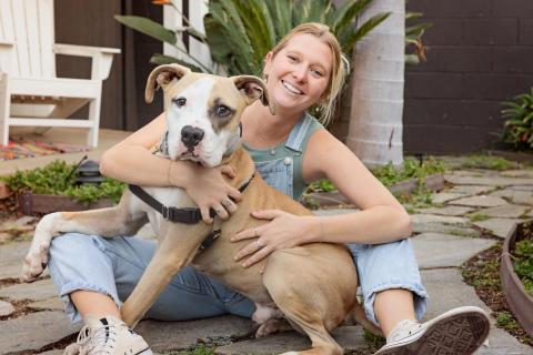 Girl smiling and sitting, holding her dog.