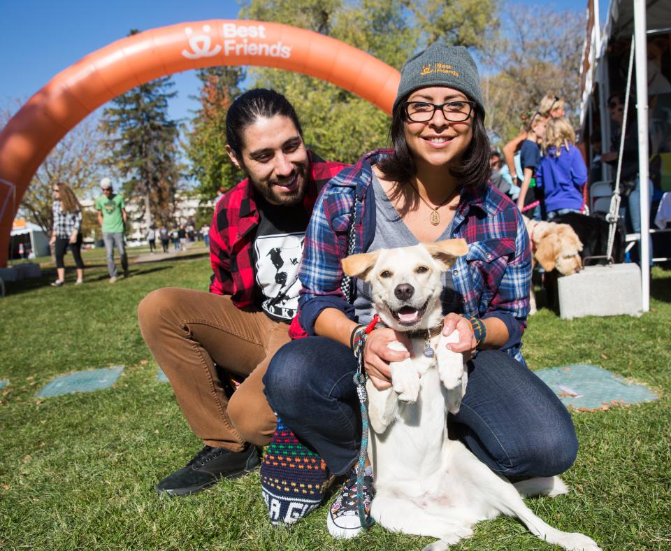 Two happy people sitting with a dog in the grass at an outdoor event