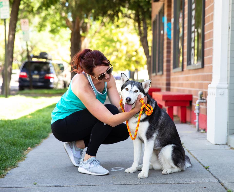 Smiling person kneeling down next to a happy leashed dog on a sidewalk