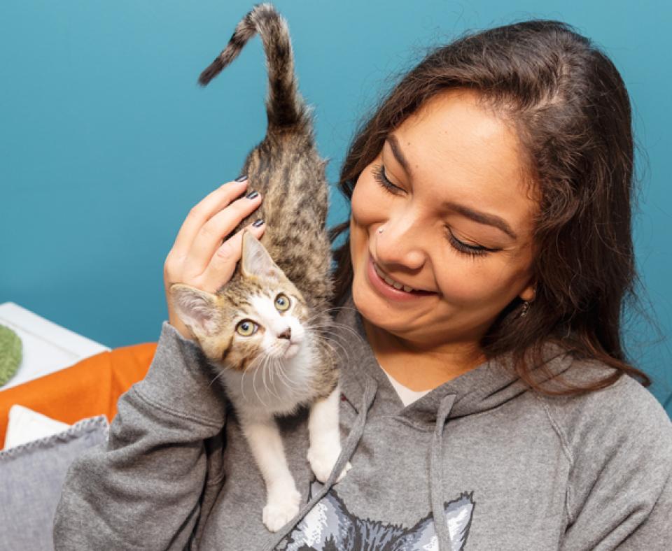 Smiling person petting a kitten who is standing on her shoulder and chest