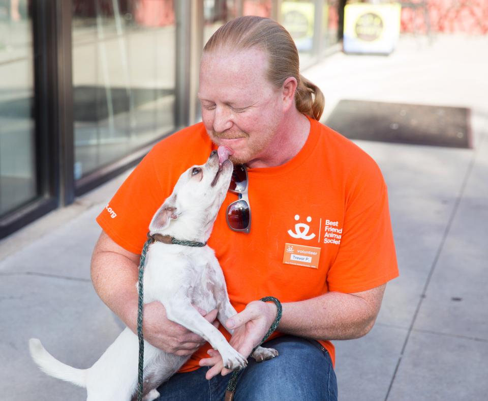 Person wearing a Best Friends orange T-shirt being kissed on the face by a small white dog