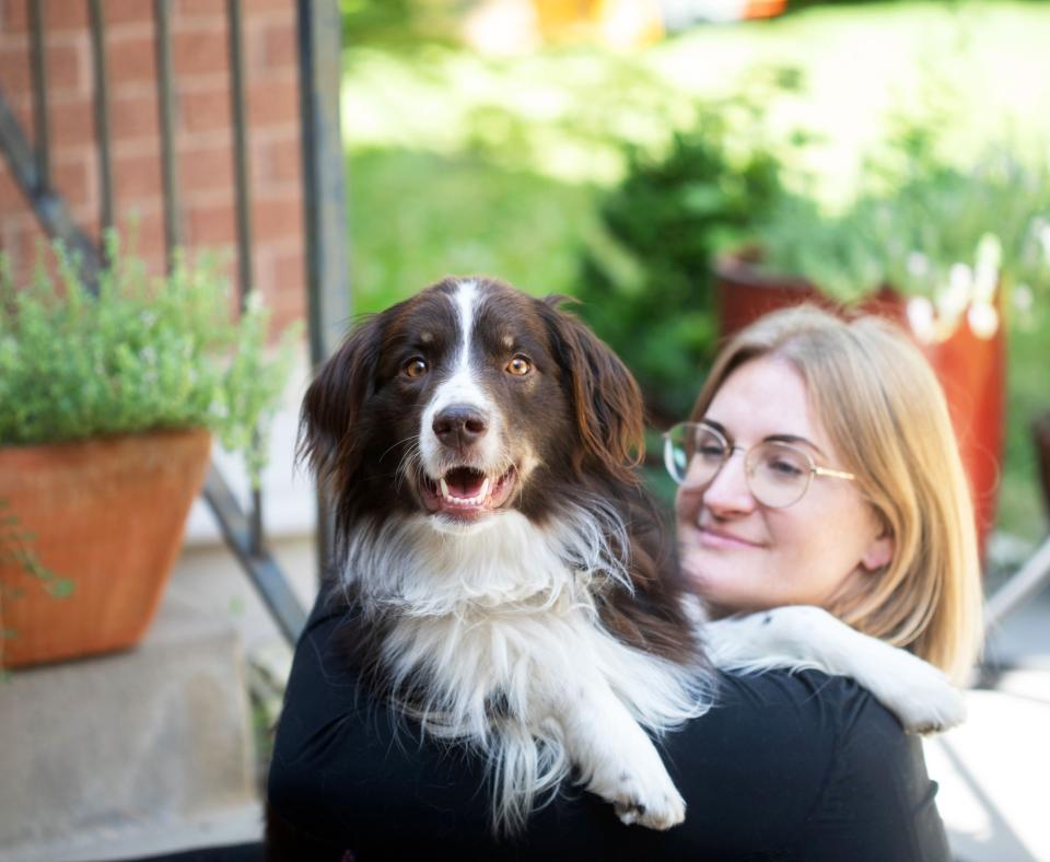 Smiling person outside with a brown and white dog whose paws are over her shoulder