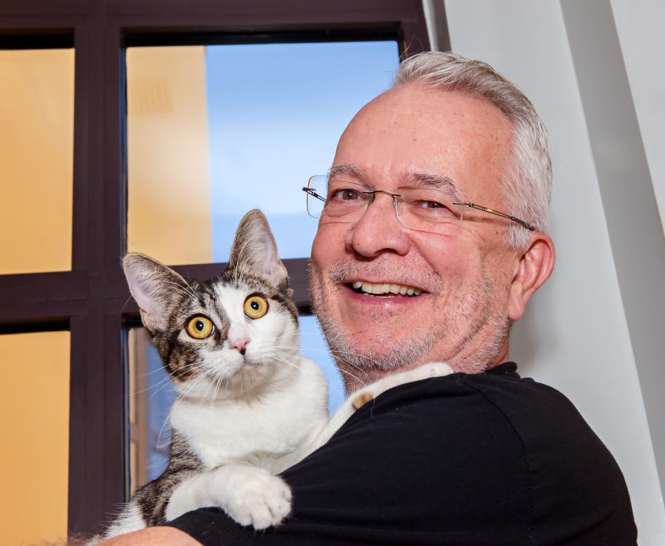 Smiling person holding a white and tabby cat in front of a window