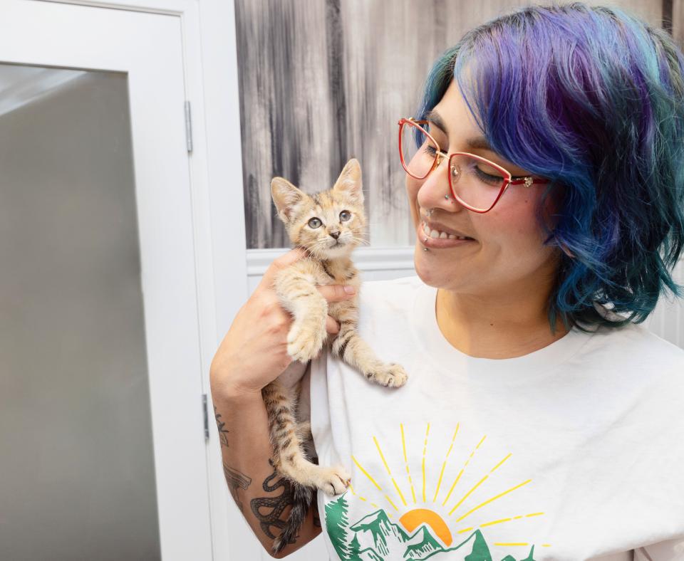 Smiling person with multi-colored hair holding a kitten