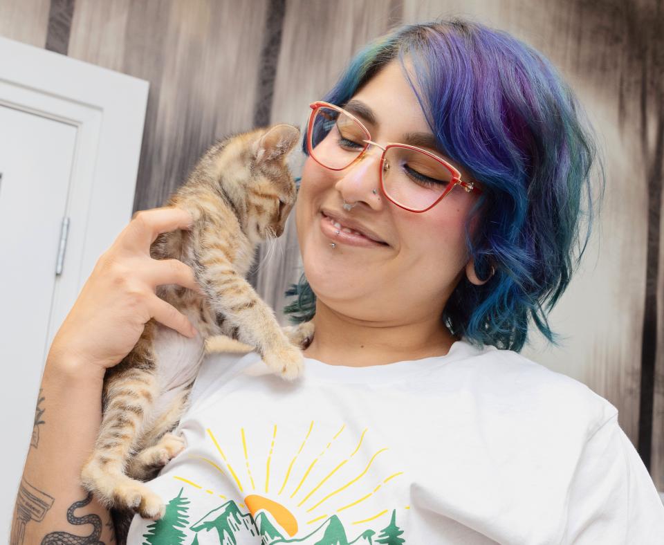 Smiling person with multi-colored hair holding a tabby kitten