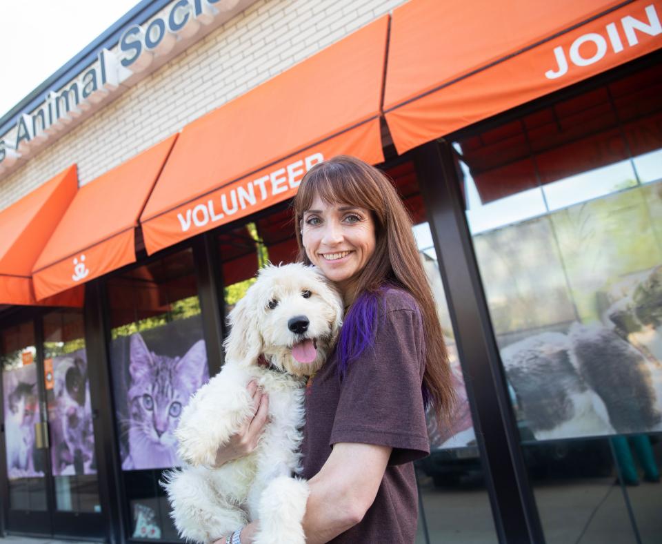 Smiling person holding a small white dog in front of a Best Friends regional location