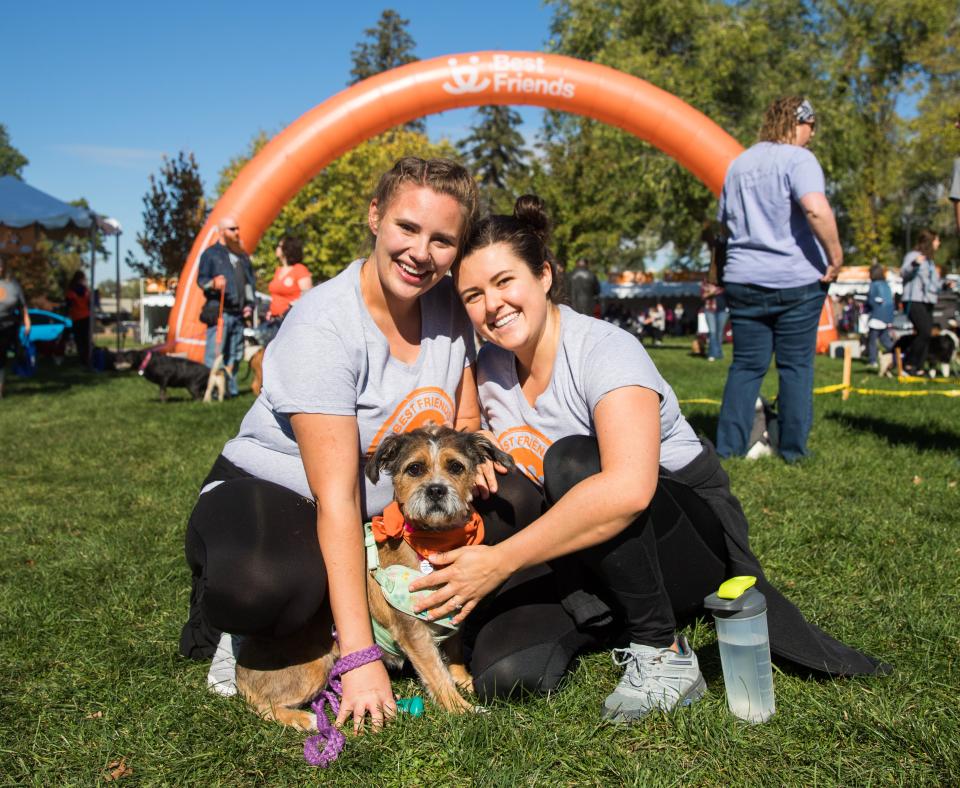 Two smiling people sitting with a dog in the grass at Strut Your Mutt in Salt Lake City