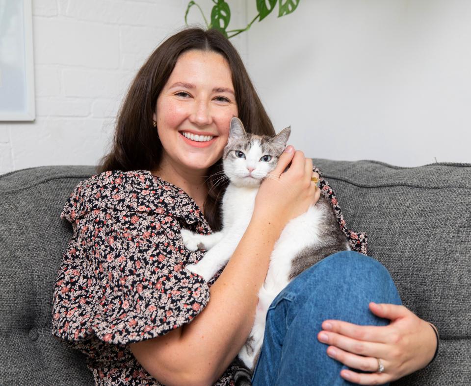 Smiling person holding a cat while sitting on a couch