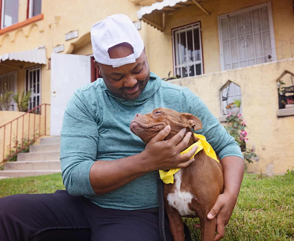 Smiling person cradling a small brown and white dog in his arms in front of a home