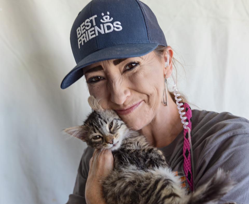 Smiling person wearing a hat cradling a tabby cat
