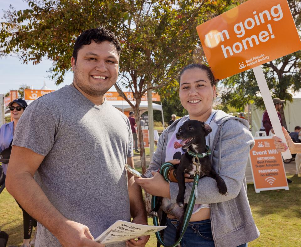 A man and woman holding their newly adopted black puppy along with a sign that says "I'm going home"