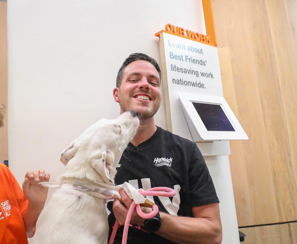 Alex Bowman smiling and getting kissed on the face by a large white dog