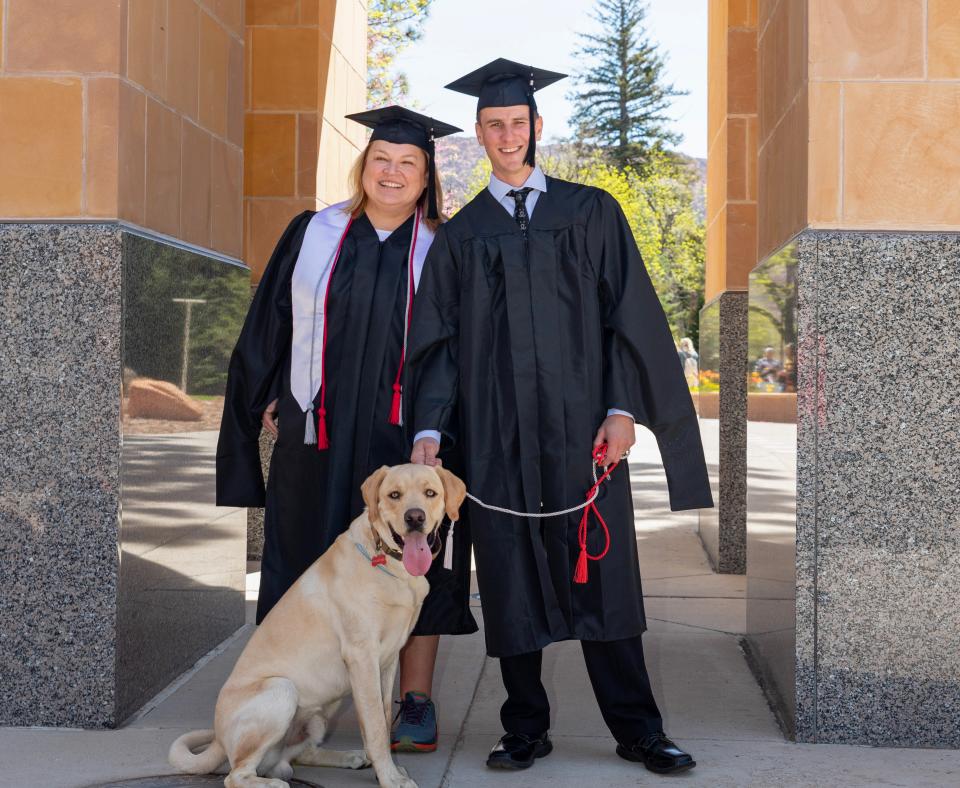 Two graduates from SUU wearing caps and gowns with a dog on a leash