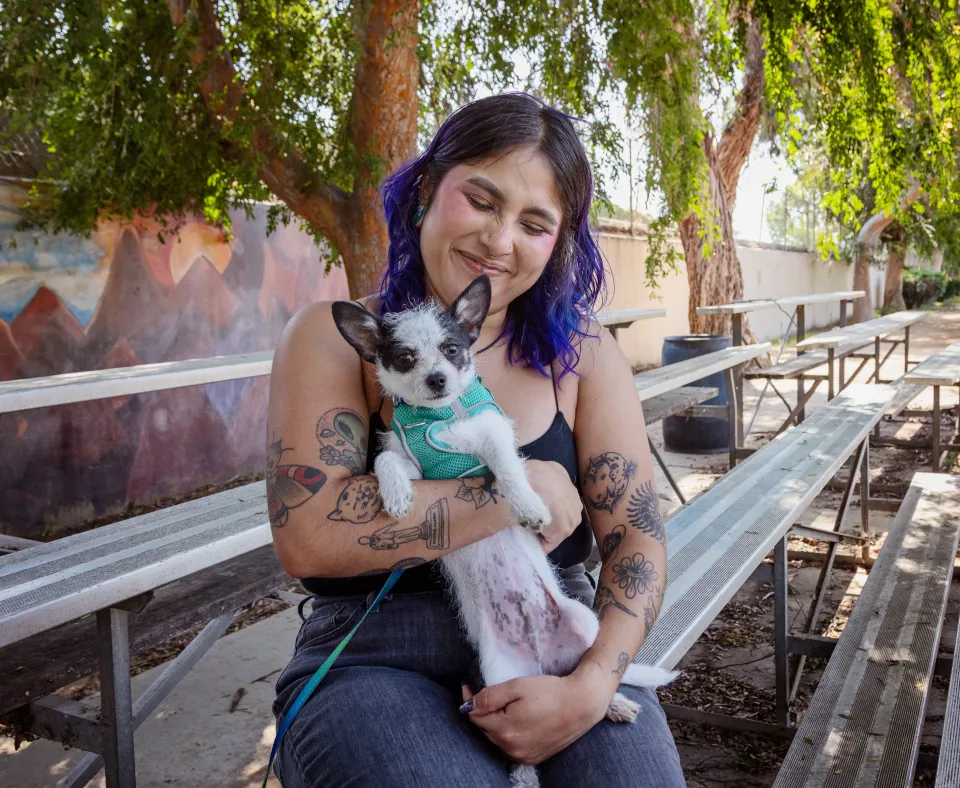 Smiling person holding a small dog in their arms while sitting outside