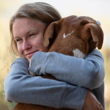 Person hugging a dog with her arms wrapped around the dog's neck