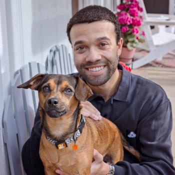 Man sitting outside on porch holding small brow dog
