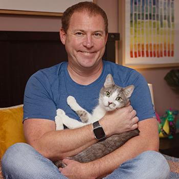 Smiling person cradling a gray and white cat in a home environment