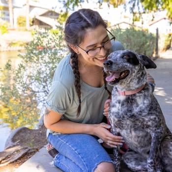 Young woman smiling warmly at her dog along a sunny canal.