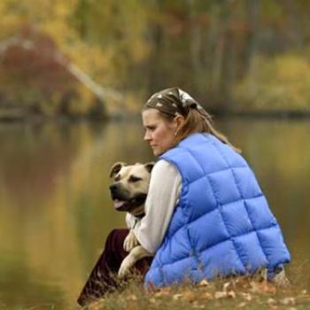 Woman sitting by lake with large dog in arms in Autumn