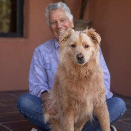 Older man sitting behind a scruffy yellow dog