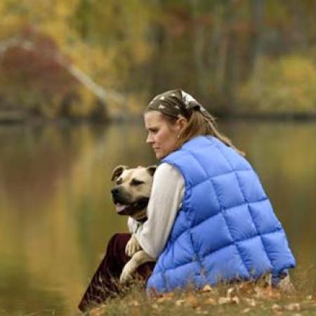 Woman sitting by lake with large dog in arms in Autumn