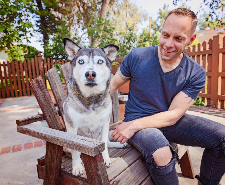 Smiling person sitting with a big dog in a chair on a patio