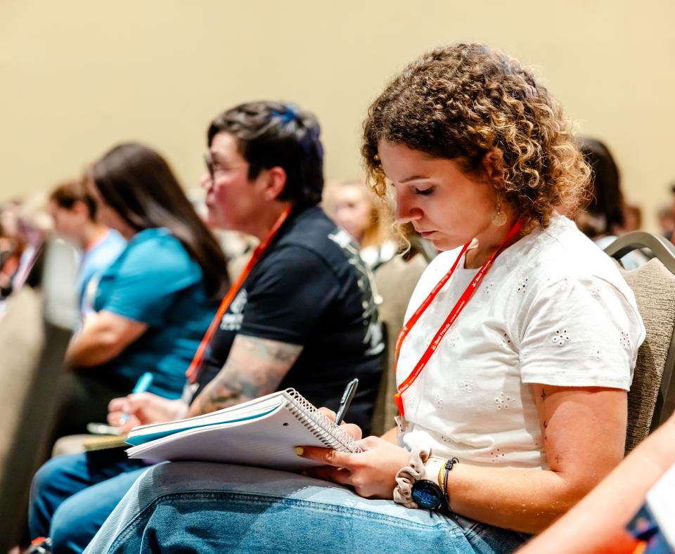 People sitting in a crowd listening to a speaker and taking notes