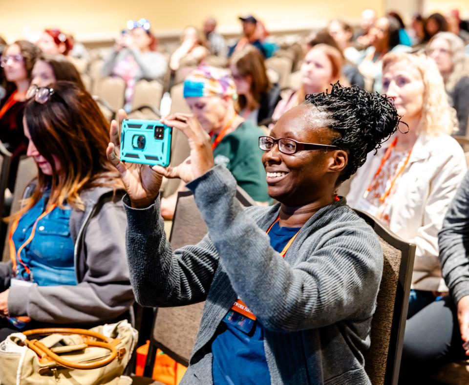 Smiling person in a crowd holding up their phone to take a photo