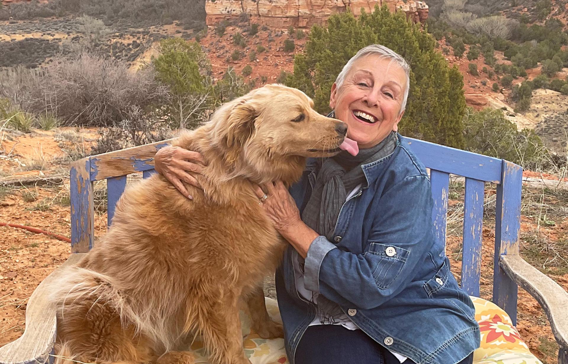 Anne Mejia on a bench in Angel Canyon with a dog who is licking her face