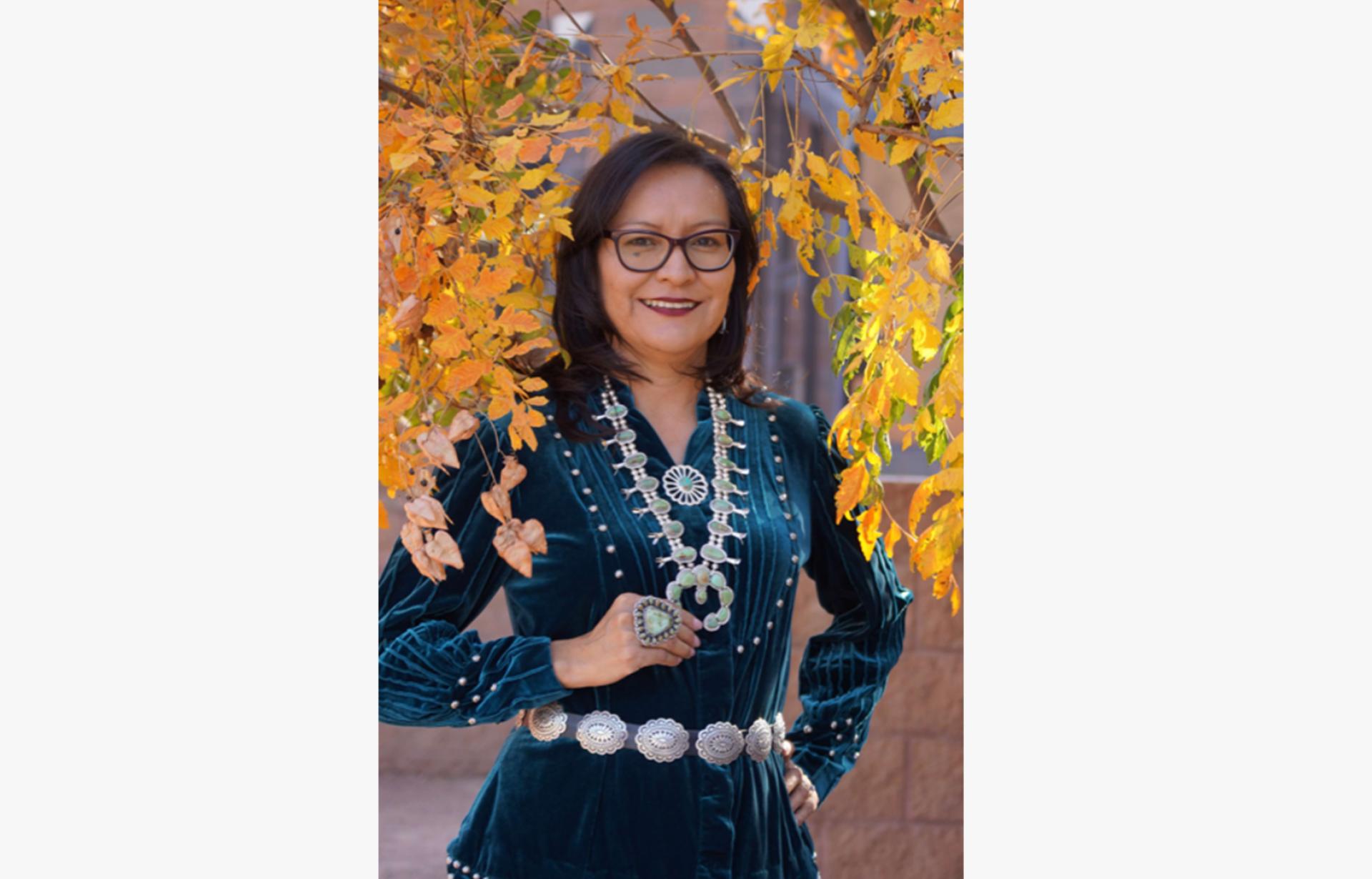 Phefelia Nez in front of a tree with yellow leaves, wearing an ornate dress and jewelry