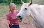 Best Friends Animal Society co-founder Diana Asher outside with a white horse whose mouth is open