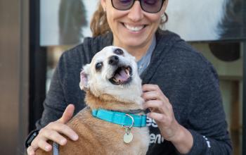 woman with small smiling dog outside on sidewalk