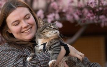 Woman holding tabby cat in front of tree with pink flowers