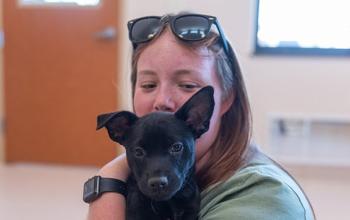 Woman with sunglasses on her head holding a small black puppy
