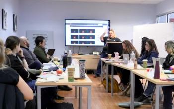A group of people gathered around a table watching a presentation