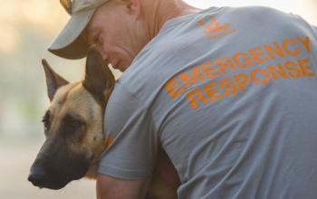 Tan dog being held by man in grey emergency response shirt