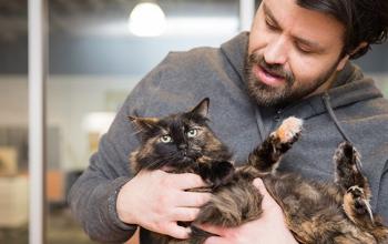 Man cradling his medium hair tortoiseshell cat in his arms