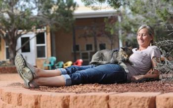 Woman lying in sand with cat on abdomen