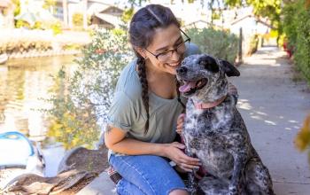 Young woman smiling warmly at her dog along a sunny canal.