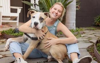 Girl smiling and sitting, holding her dog.