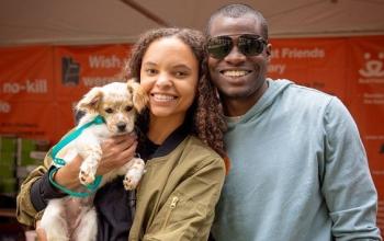 Man in gray sweatshirt standing next to woman in green jacket holding small dog