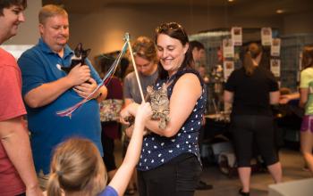 woman in a group holding cat with cat toy 